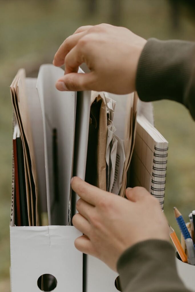 pexels-photo-6636324 Hands arranging papers and notebooks in a box, highlighting organization and office work.